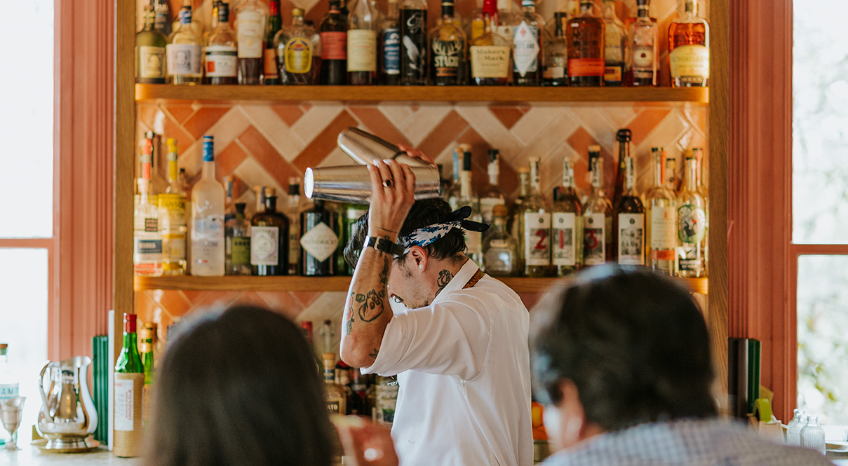 A bartender shaking a cocktail with two guests at Hannah's Bar